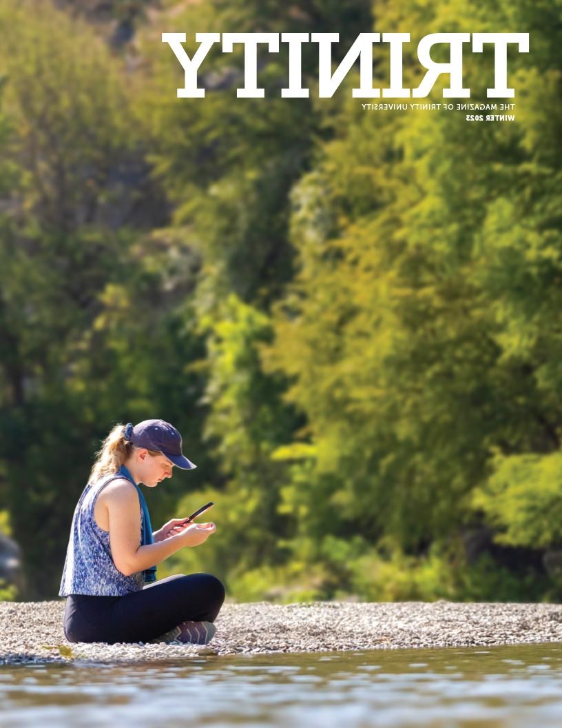 the cover of the Winter 2023 Trinity magazine fratures a person siting on rocks next to water looking through a magnifying glass