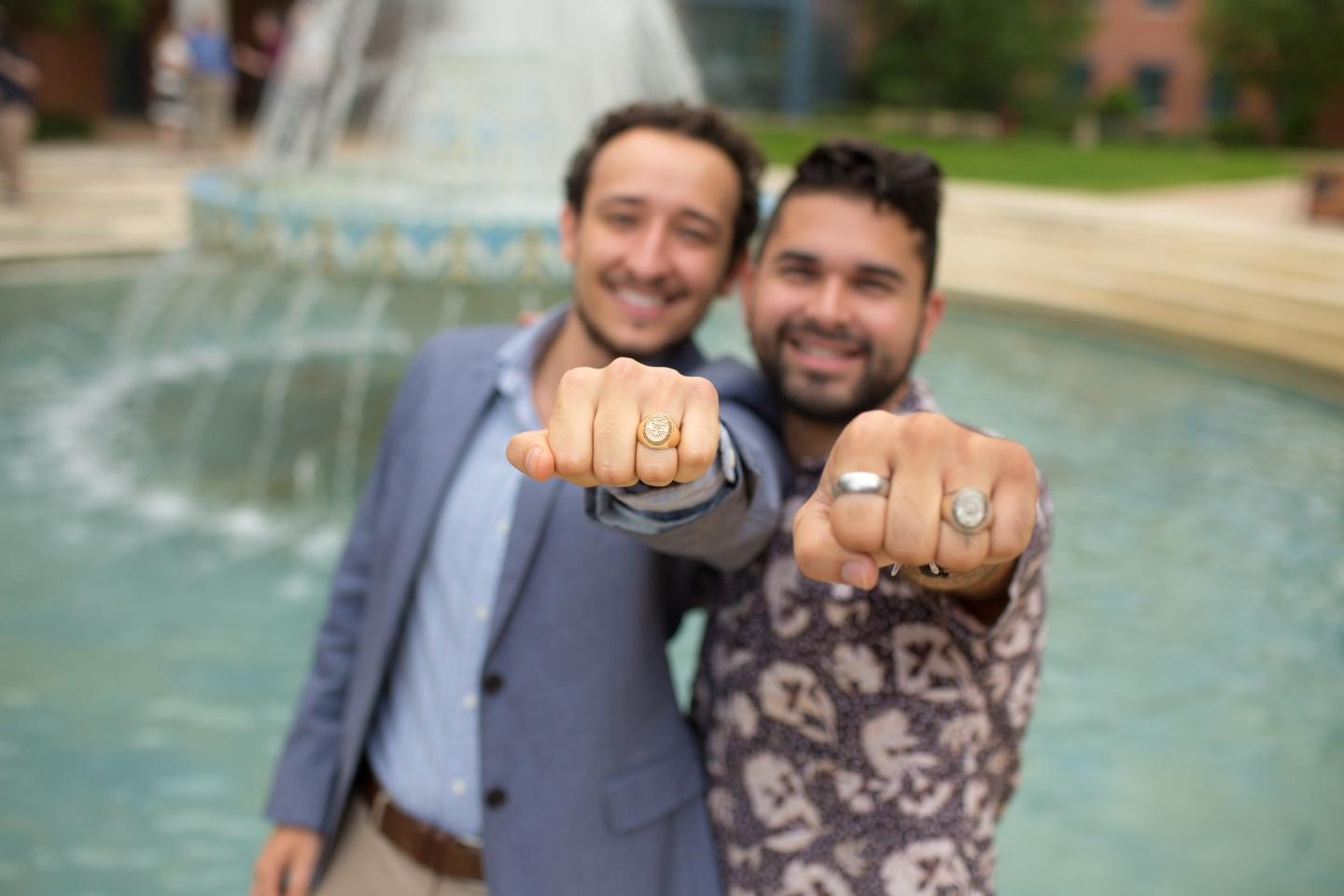 two students show off their class rings next to miller fountain